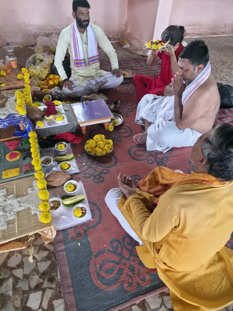 Guruji seated with a family during their puja, kalash and offerings laid out
