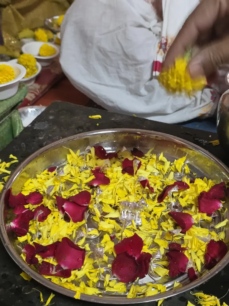 Rose and marigold petals over silver offerings in the puja thali